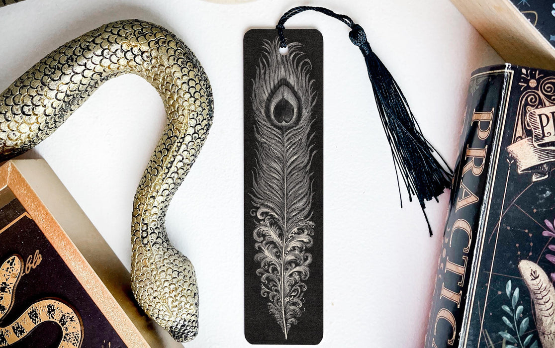 a black feather bookmark with a decorative tassel, placed next to a book and a snake decoration.