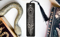 a black feather bookmark with a decorative tassel, placed next to a book and a snake decoration.