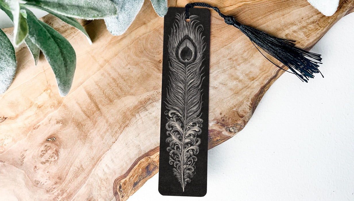 A black and white feather bookmark with a tassel is placed on a wooden surface, accompanied by a green plant leaf.