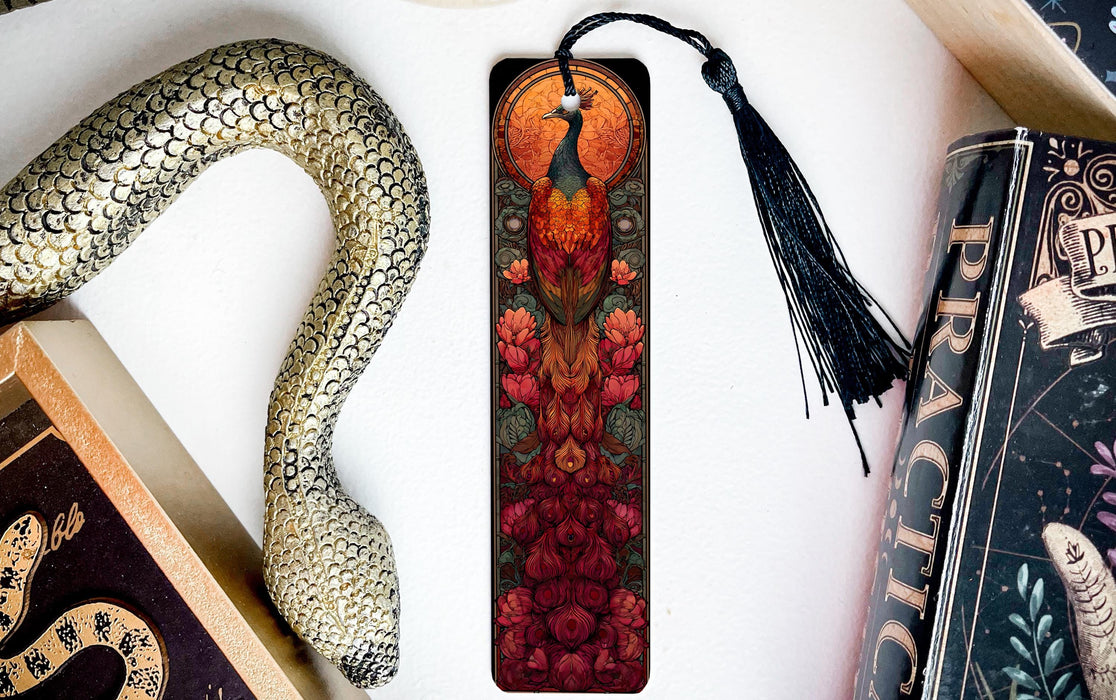 a decorative bookmark with a peacock design, placed on a white surface next to a book and a snake-shaped object.