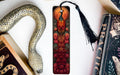 a decorative bookmark with a peacock design, placed on a white surface next to a book and a snake-shaped object.