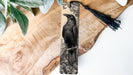 A wooden surface with a black and white illustration of a bird perched on a branch, accompanied by a black tassel.