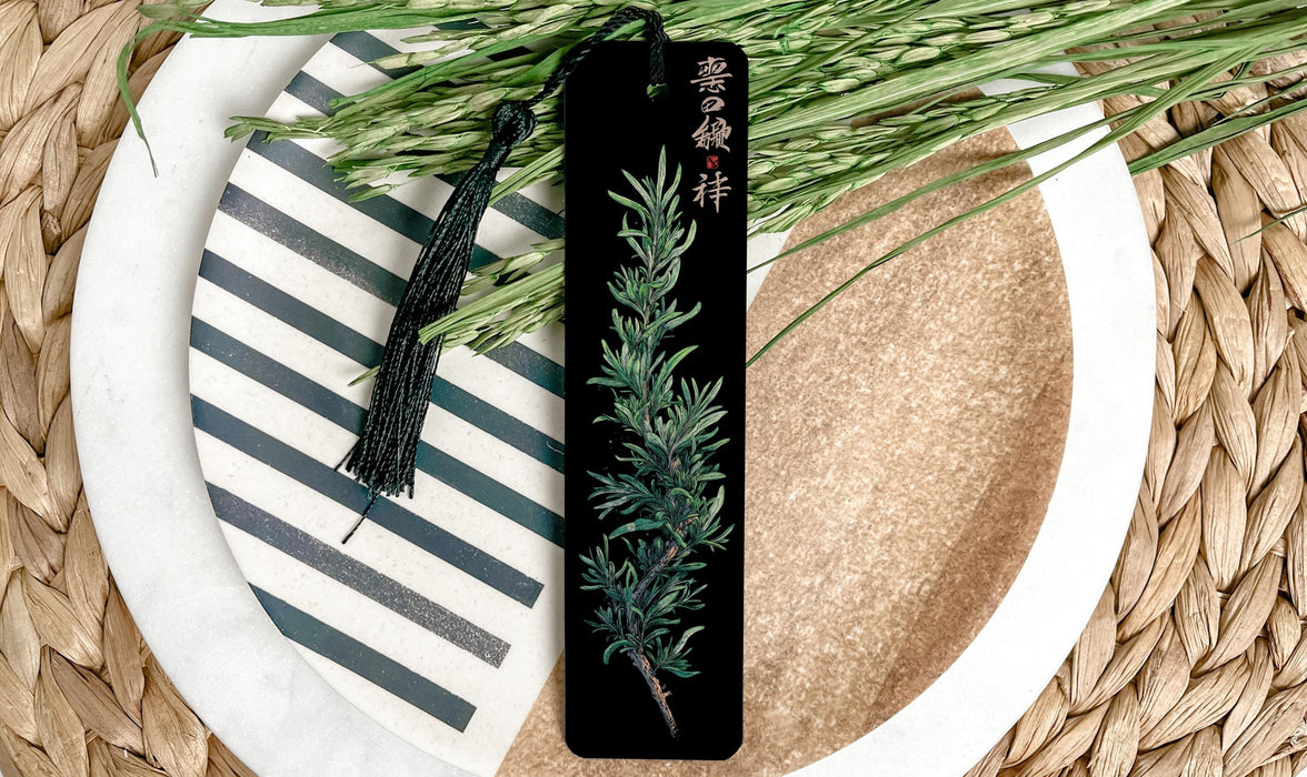 A black bookmark with a green plant design rests on a white plate with a black and white striped pattern.