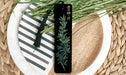 A black bookmark with a green plant design rests on a white plate with a black and white striped pattern.