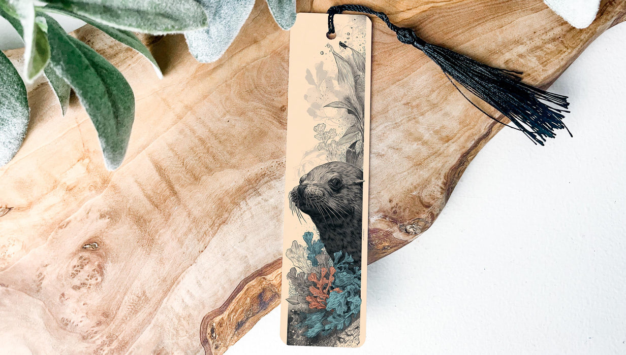 A wooden bookmark with a black tassel attached, featuring an illustration of a seal or sea lion.