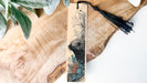 A wooden bookmark with a black tassel attached, featuring an illustration of a seal or sea lion.