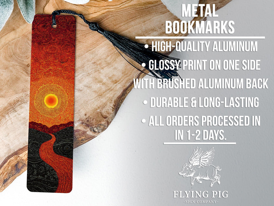 a metal bookmark with a vibrant design, including a sun and a winding path, resting on a wooden surface.