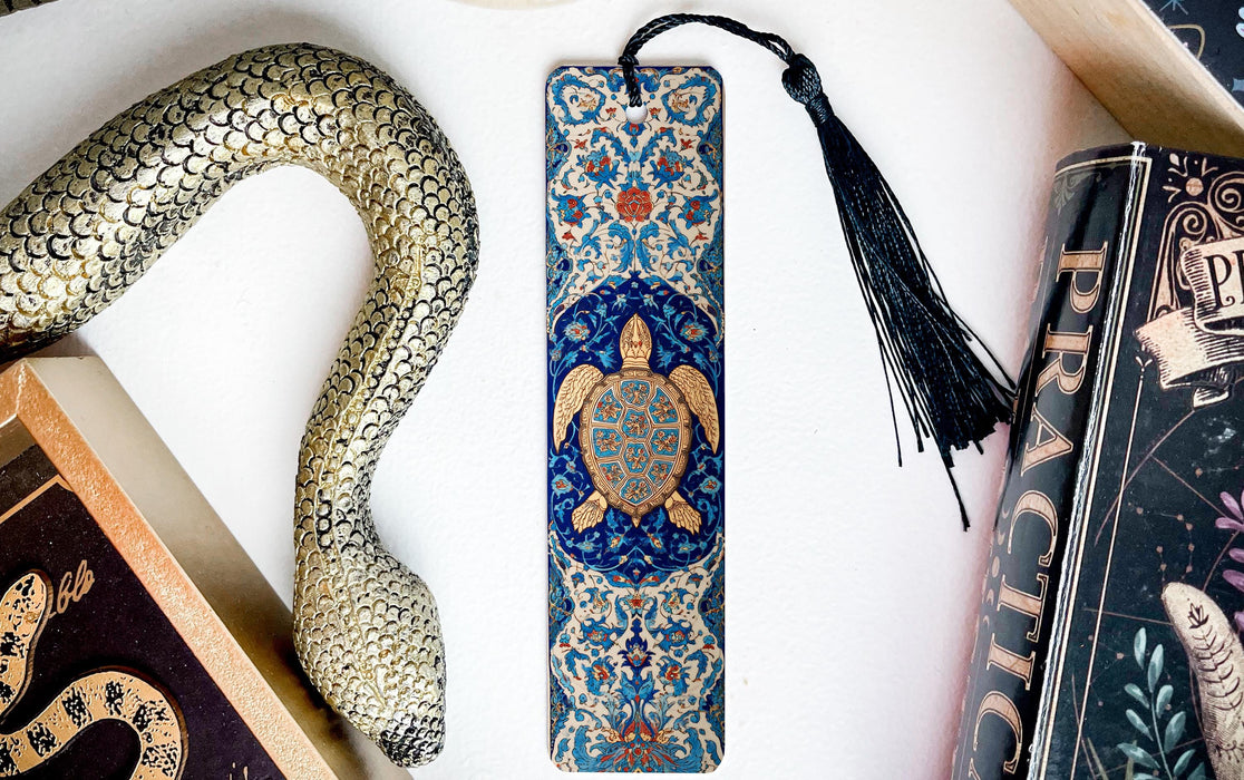 A decorative snake-shaped bookmark with a blue and gold design, a black tassel, and a book titled "PRACTICAL" are displayed on a white surface.