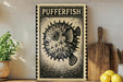 a framed artwork of a pufferfish on a shelf, with a wooden cutting board and a potted plant to the side.