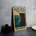 A vintage metal sign with the text "PULPIT ROCK NORWAY" and an illustration of a cliff overlooking a river, placed on a gray countertop next to some black camera lenses.