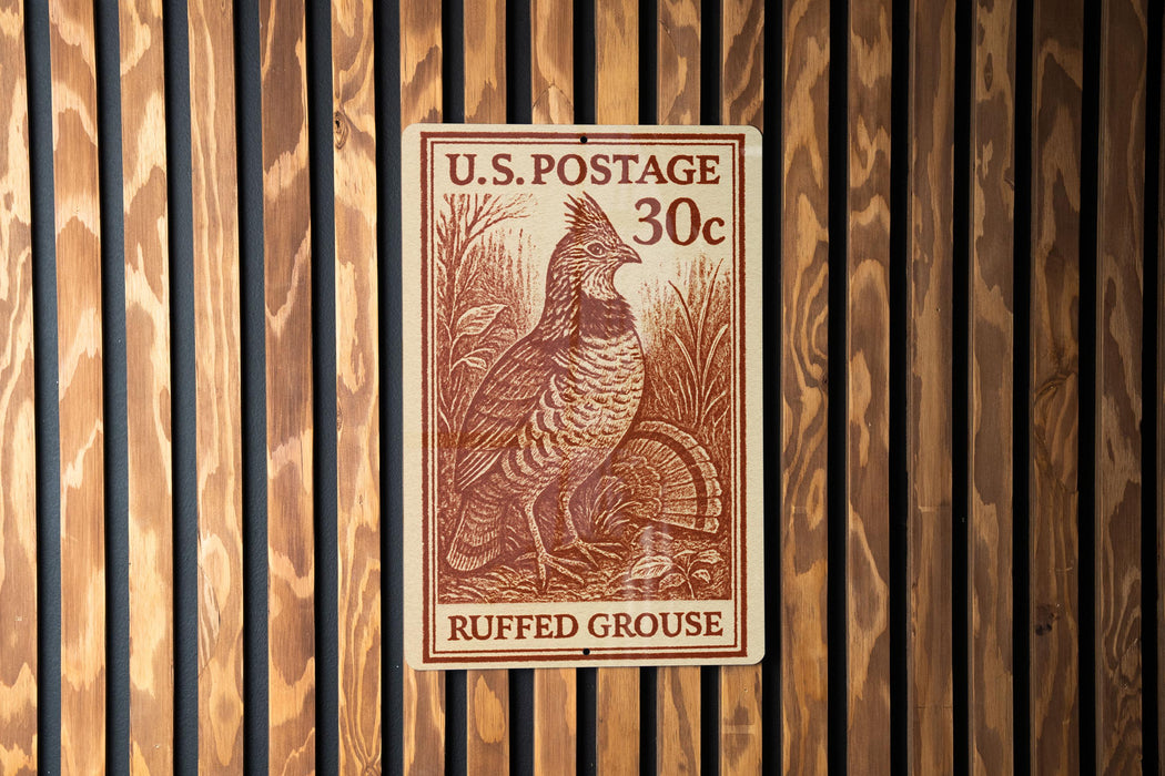 A U.S. postage stamp featuring a ruffed grouse, which is a type of bird, is displayed on a wooden wall.