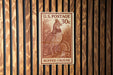A U.S. postage stamp featuring a ruffed grouse, which is a type of bird, is displayed on a wooden wall.
