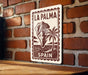 A sign with the text "LA PALMA" and "SPAIN" printed on it, mounted on a brick wall.