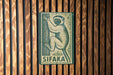 A metal sign with a monkey illustration is mounted on a wooden wall.