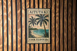 A vintage-style metal sign with a tropical beach scene and palm trees, mounted on a wooden wall.
