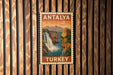 A vintage postage stamp from Turkey depicting a waterfall and mountains, mounted on a wooden wall.