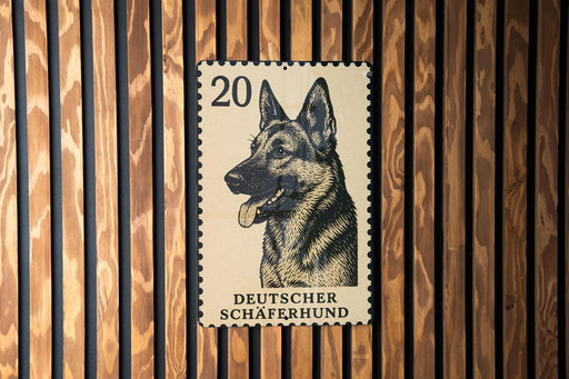 A German Shepherd dog is depicted on a German postage stamp, which is affixed to a wooden wall.