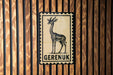 a stamp-like sign with a giraffe illustration, mounted on a wooden wall.