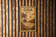 A vintage-style metal sign with the text "GOA INDIA" displayed prominently, featuring a tropical landscape with palm trees and a body of water.