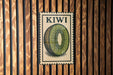 A vintage-style metal sign with the word "KIWI" printed on it, featuring a close-up illustration of a kiwi fruit slice.