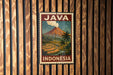 A vintage-style poster of Java, Indonesia, featuring a mountain landscape with a volcano and palm trees, is displayed on a wooden wall.