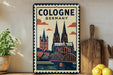 A vintage-style metal sign with a colorful illustration of the Cologne Cathedral in Germany, featuring a castle, bridge, and clouds in the background.
