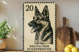 A German Shepherd dog is depicted on a German postage stamp, which is placed on a wooden surface next to a wooden cutting board and some lemons.