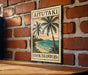 A vintage-style sign with a tropical beach scene and palm trees, mounted on a brick wall.