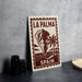 A sign for La Palma, Spain, featuring a palm tree and a mountain, is displayed on a table next to some black camera lenses.