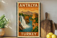 A vintage-style poster of Antalya, Turkey, featuring a waterfall and mountains, is displayed on a wall next to a wooden cutting board and a potted plant.