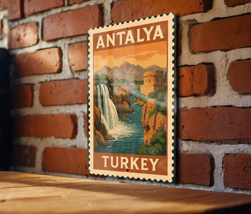 A vintage postage stamp depicting a waterfall and mountains, with the text "ANTALYA TURKEY" printed on it, is displayed on a brick wall.