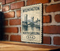 A vintage-style postage stamp featuring the Wilmington Bridge in North Carolina, United States, hanging on a brick wall.