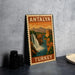 A vintage-style metal sign with the text "ANTALYA TURKEY" and an illustration of a waterfall and mountains, placed on a gray countertop next to some black camera lenses.