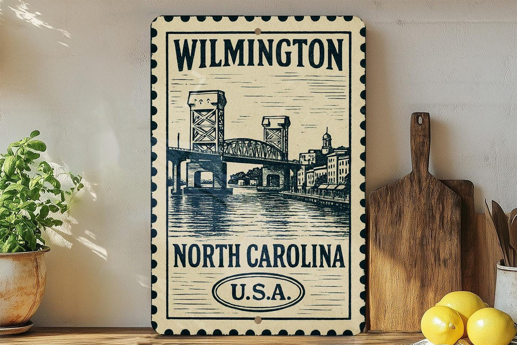 A vintage-style metal sign with a drawing of a bridge and the text "Wilmington North Carolina U.S.A." displayed on a wooden shelf.