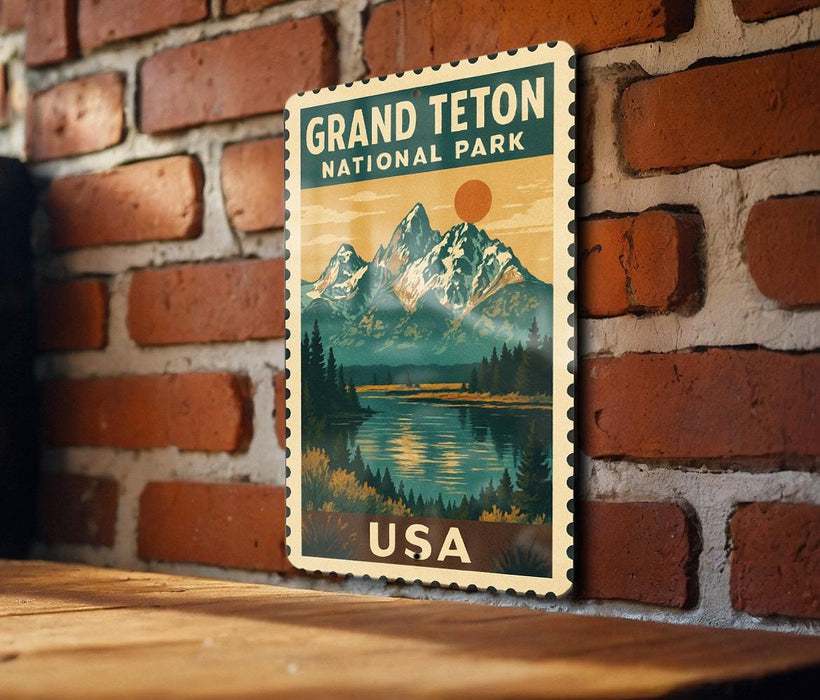 A vintage-style metal sign depicting the Grand Teton National Park in the United States, mounted on a brick wall.