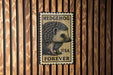 A metal stamp with a hedgehog image and the text "HEDGEHOG USA FOREVER" is displayed on a wooden wall.