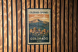 A vintage-style postage stamp from Colorado Springs, USA, featuring a mountain landscape and a cityscape.