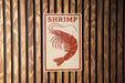 A sign with the word "SHRIMP" written on it, depicting a shrimp.