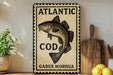 A decorative sign featuring a fish and the text "ATLANTIC COD GADUS MORHUA" is displayed on a wooden shelf next to a potted plant and a cutting board.