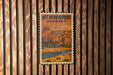 a vintage-style poster of a Moroccan city, with a mountain in the background and palm trees, displayed on a wooden wall.