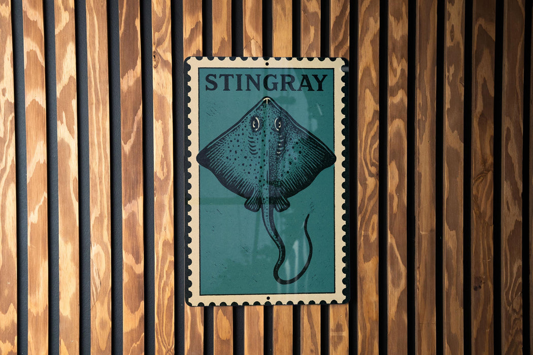 A metal sign with a blue background and a graphic of a stingray is mounted on a wooden wall.