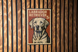 A Labrador Retriever dog is depicted on a postage stamp-like sign, which is mounted on a wooden wall.