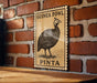a wooden table with a vintage-style postage stamp depicting a guinea fowl, mounted on a brick wall.