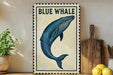 a framed illustration of a blue whale on a shelf, with a wooden cutting board and a potted plant to the side.
