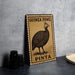 A metal sign with a printed image of a guinea fowl and the text "GUINEA FOWL PINTA" is displayed on a table.
