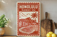 A vintage-style sign depicting a tropical beach scene with palm trees, mountains, and a body of water, with the text "HONOLULU, HAWAII USA" prominently displayed.