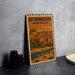 A vintage metal sign with an illustration of a Moroccan city, featuring a mountain and a river, is displayed on a table.