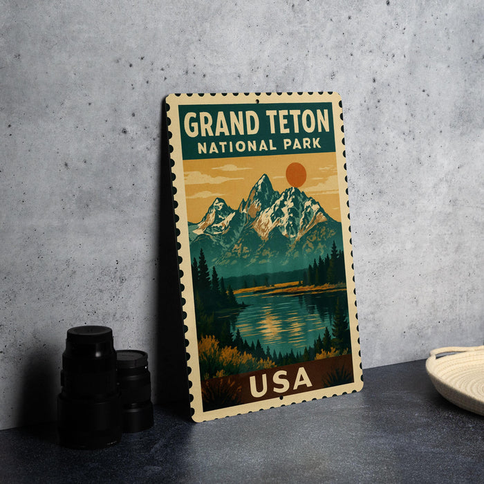 A vintage-style postage stamp featuring a scenic landscape with mountains, a lake, and a sunset, with the text "GRAND Teton NATIONAL PARK USA" printed on it.