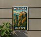 A vintage-style metal sign with the text "METEORA GREECE" displayed on a wall, featuring a scenic mountain landscape with a castle-like structure.