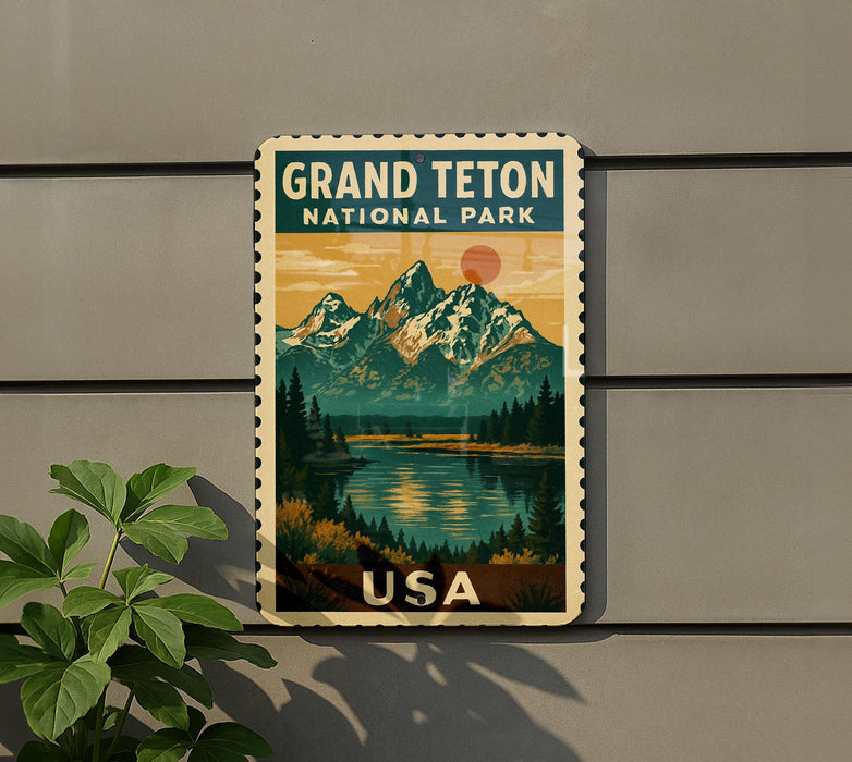 A vintage-style postage stamp featuring a mountain landscape with a lake and pine trees, mounted on a wall next to a plant.